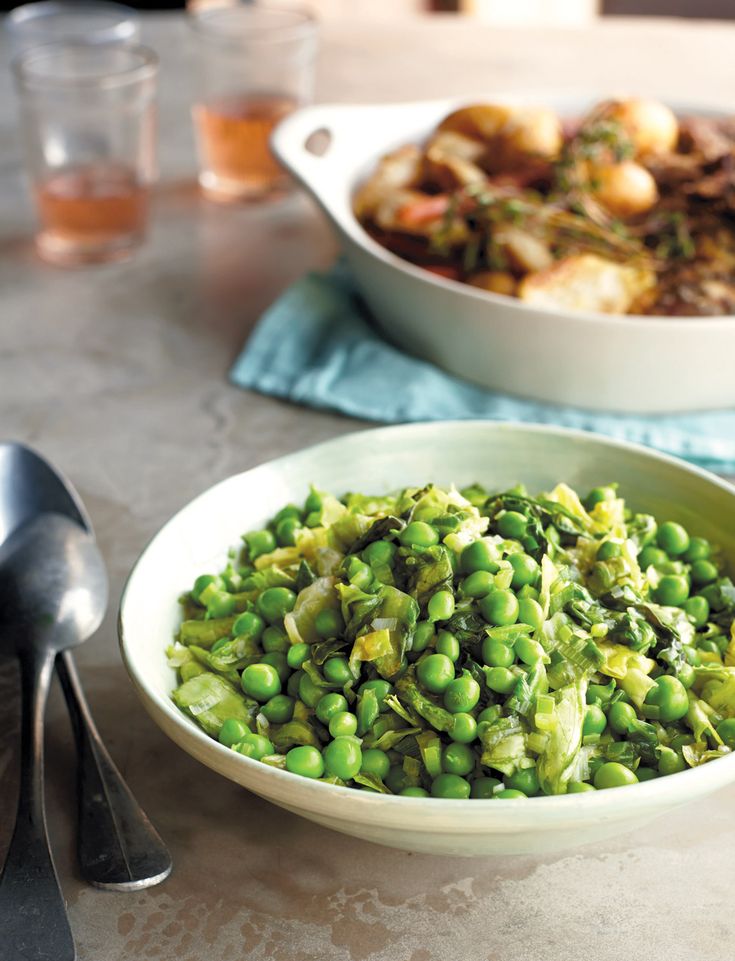 a white bowl filled with green peas next to a plate of food on top of a table