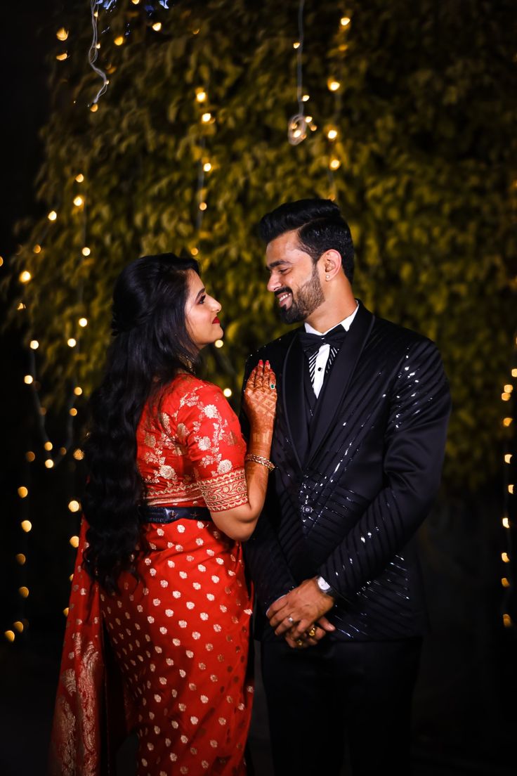 a man and woman standing next to each other in front of trees with lights on them