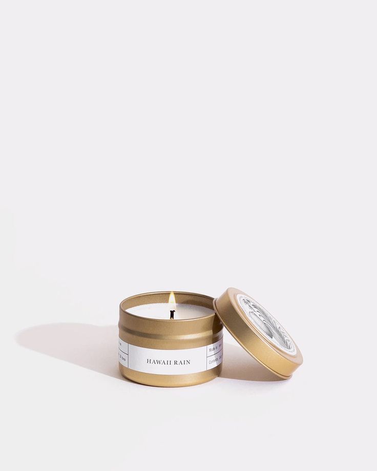 a candle that is sitting in front of a white background with a gold tin on it