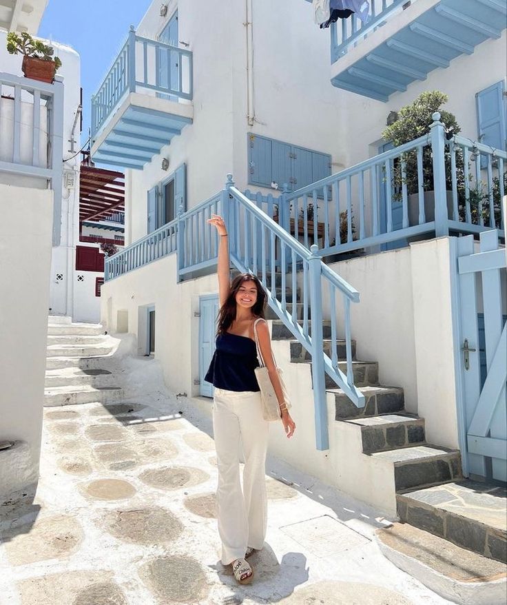 a woman standing in front of some blue and white buildings holding her hand up to the sky