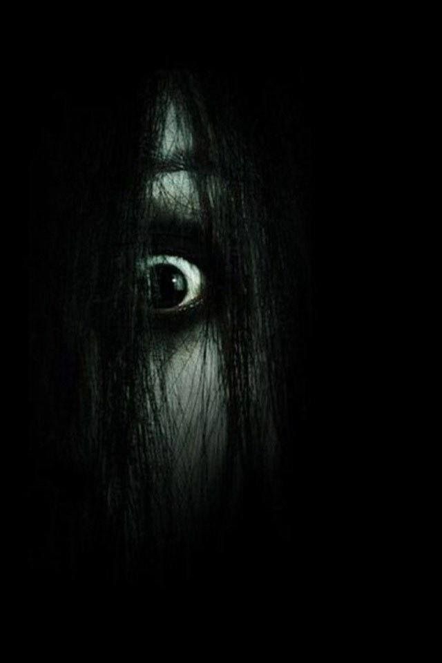 an evil looking woman's eye is seen in this dark photo with long black hair