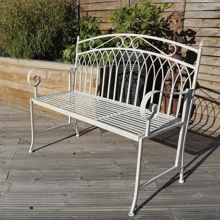 a white metal bench sitting on top of a wooden deck next to a building and potted plants