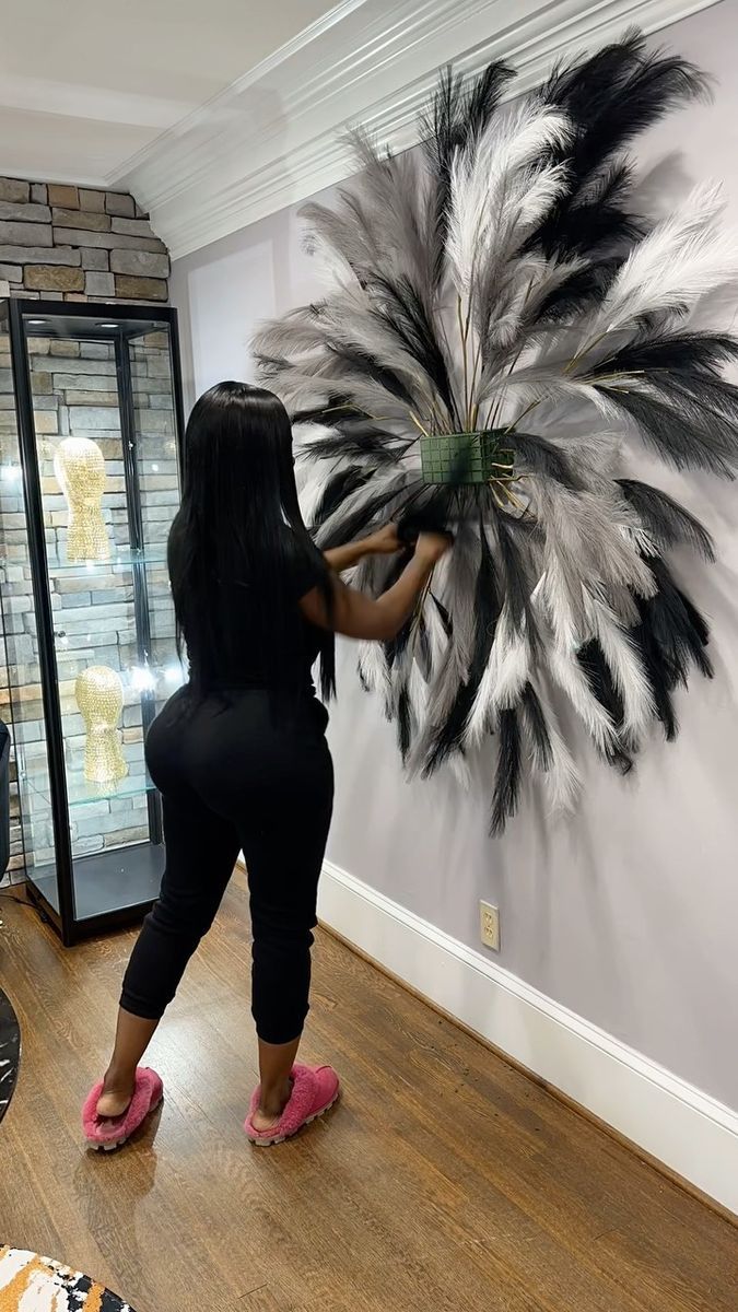 a woman standing in front of a large feathered wall hanging on the side of a building