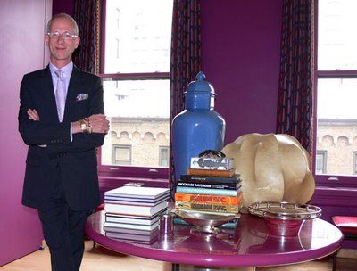 a man in a suit standing next to a table with books and vases on it