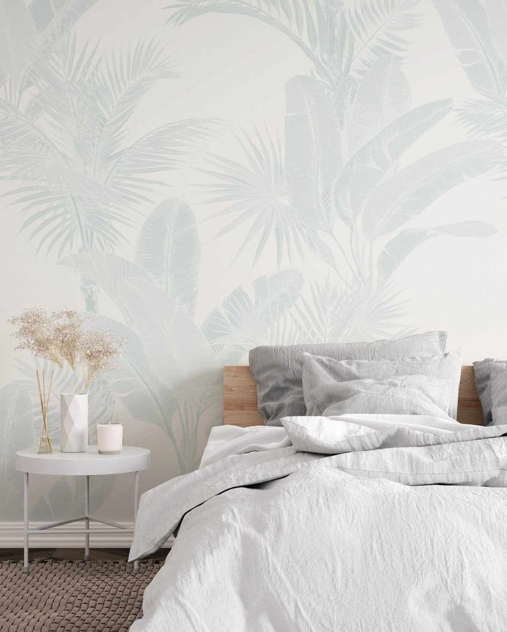 a bed with white sheets and pillows in front of a palm tree wallpaper