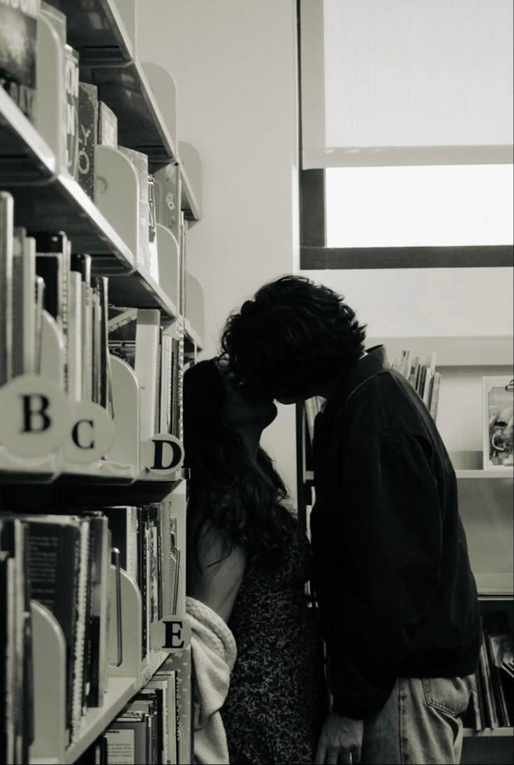 a man and woman kissing in front of a book shelf with books on the shelves