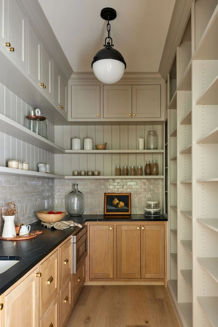 a kitchen with wooden cabinets and black counter tops, white shelves and light wood flooring