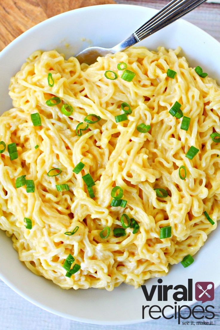 a white bowl filled with noodles and scallions on top of a wooden table