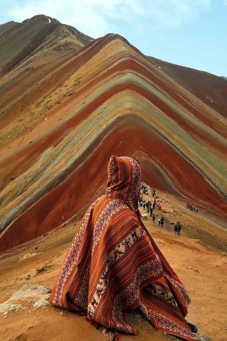 a woman sitting on top of a hill covered in a colorful blanket and covering her face