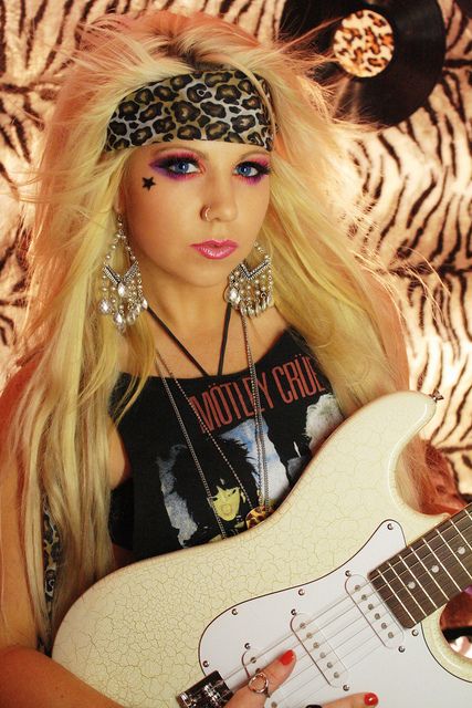 a woman with long blonde hair holding a white guitar in front of a zebra print background