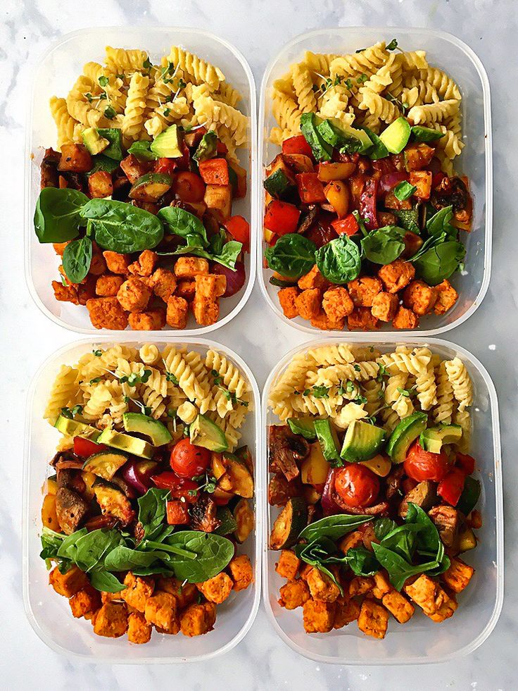 four plastic containers filled with different types of pasta and veggies on top of a marble table