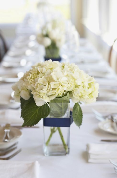 there is a long table with white flowers in the center and place settings on it