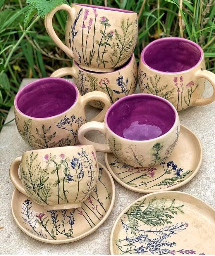 the purple cups and saucers are sitting on the table next to each other with flowers painted on them