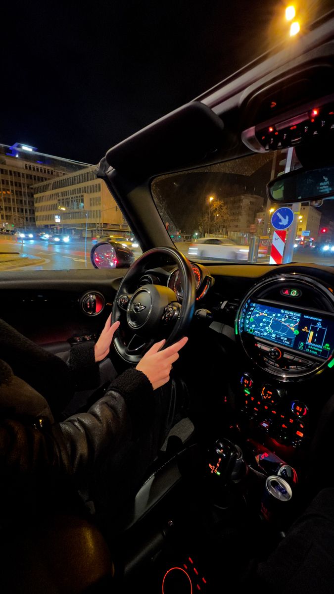 a man driving a car at night in the city with his hands on the steering wheel