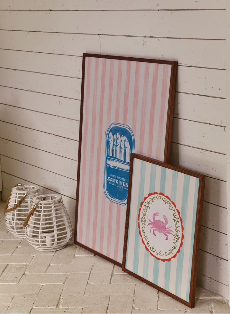 two framed pictures sitting next to each other on a brick floor in front of a white wall