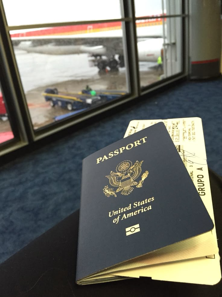 two passports sitting on top of each other in front of an airport window with the door open