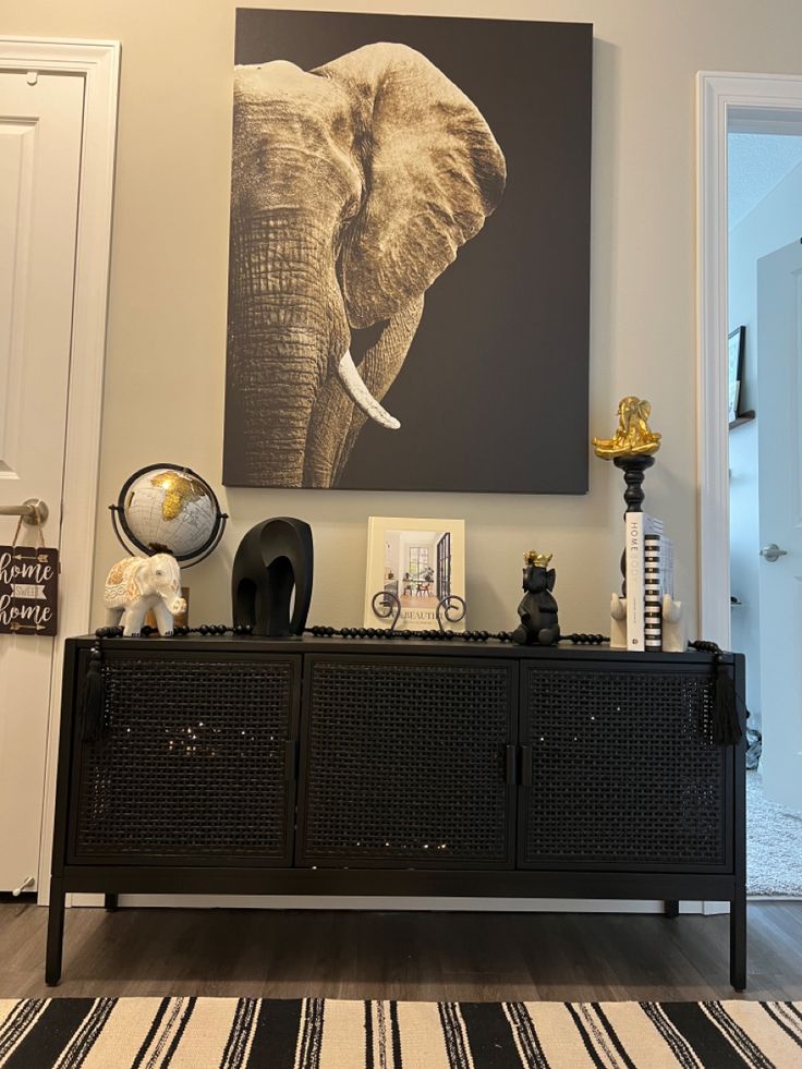 an elephant painting is on the wall above a black sideboard in a living room