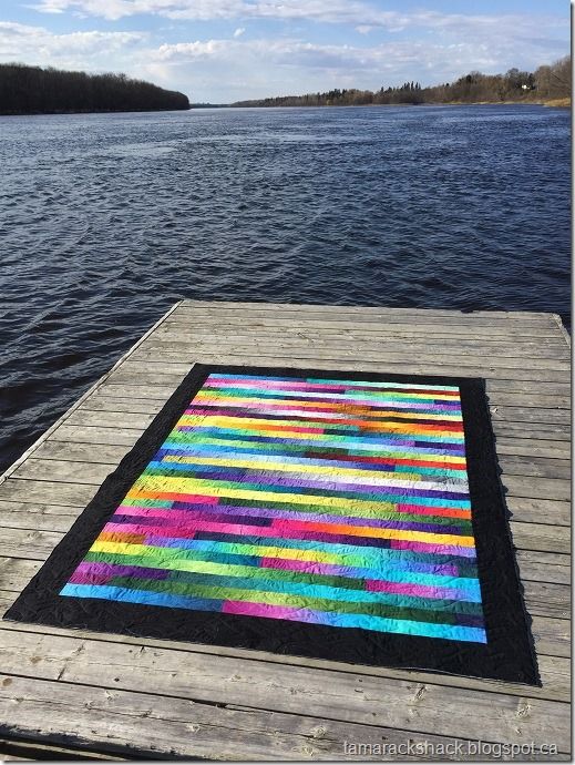 a multicolored rug sitting on top of a wooden pier next to the water