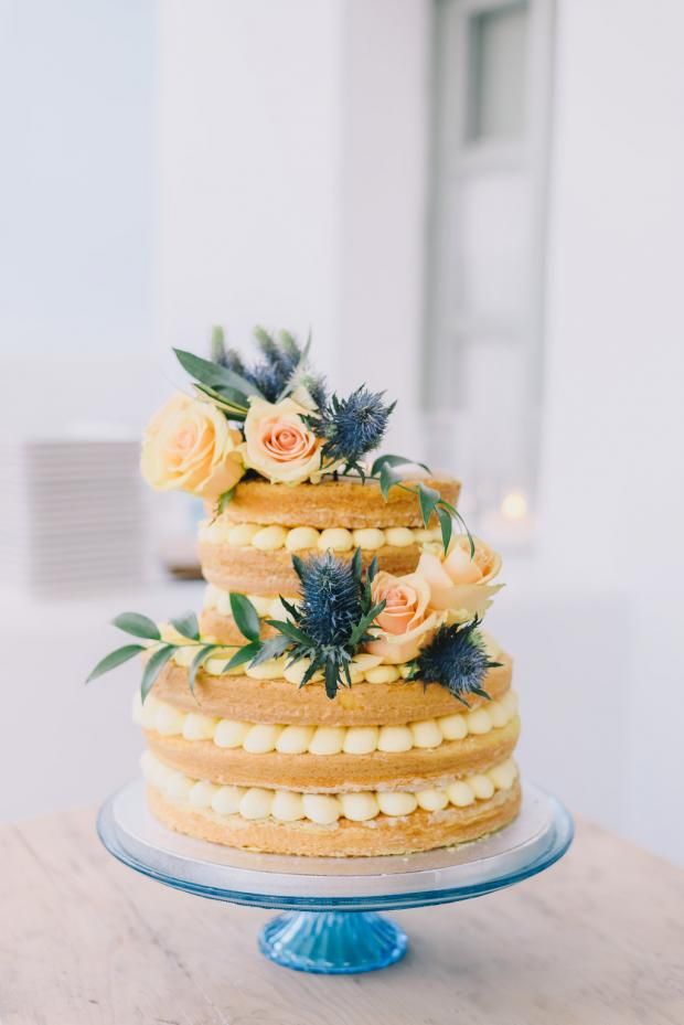 a three tiered cake with flowers on top sits on a blue plate in front of a white wall