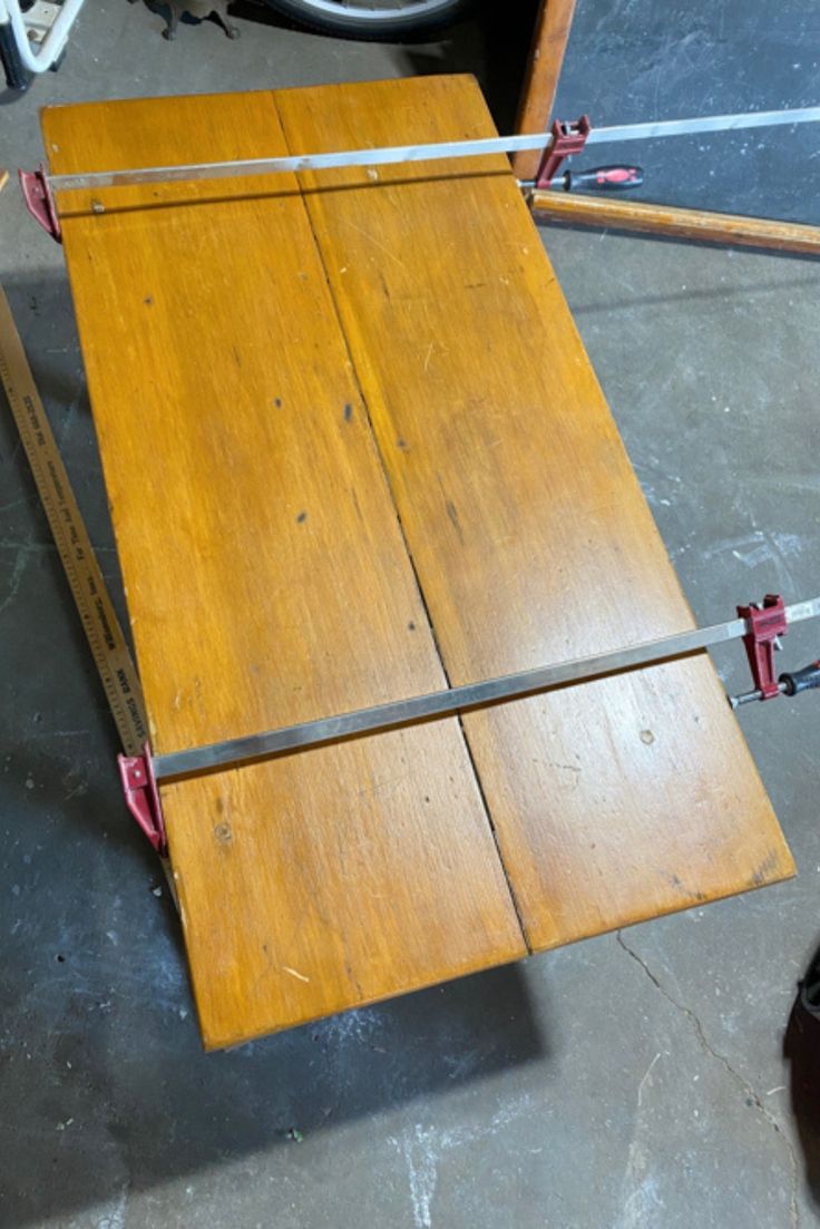 a wooden table sitting on top of a floor next to a pair of red shoes