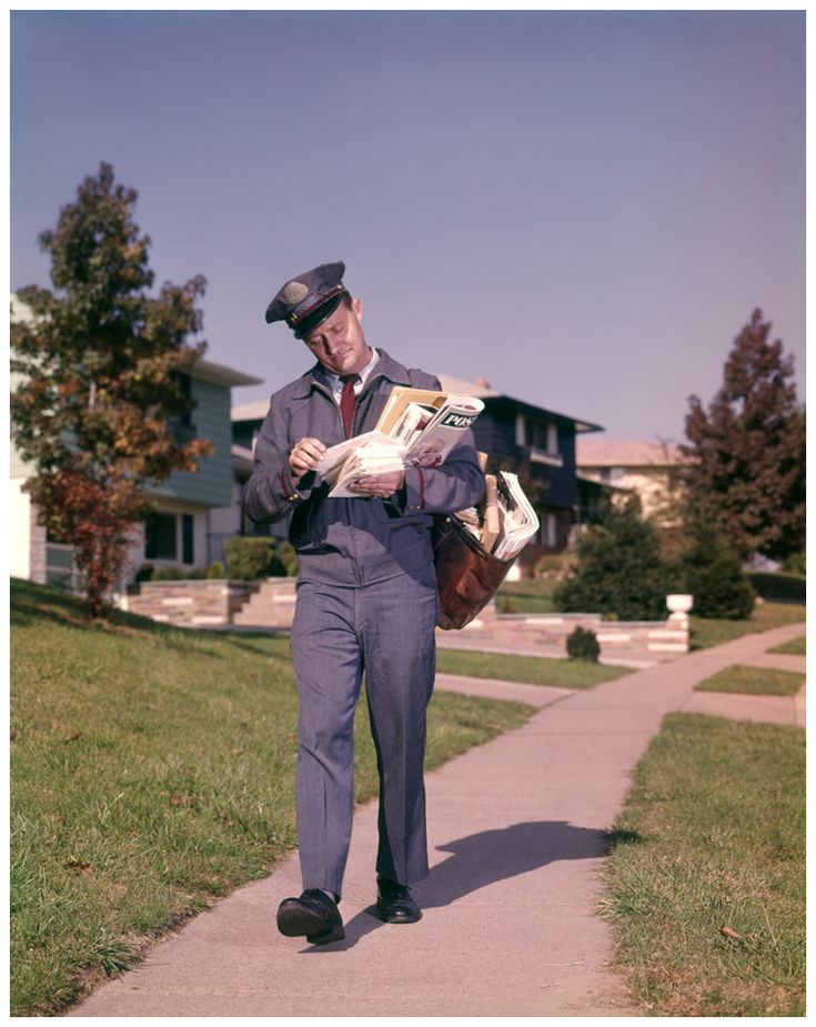 a man in a suit and hat walking down a sidewalk while reading a news paper