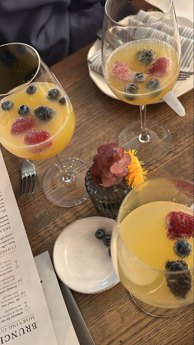 two wine glasses filled with fruit on top of a wooden table next to a menu