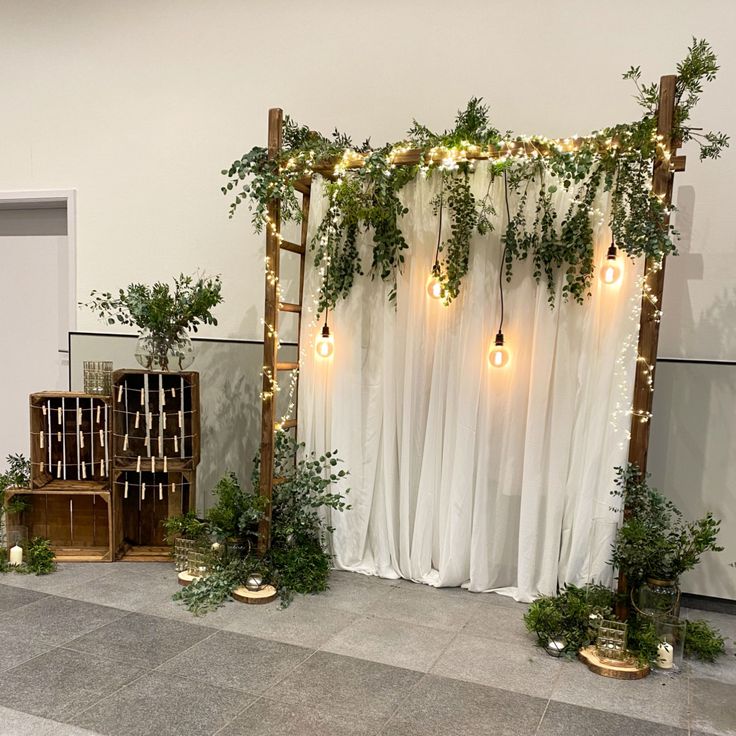 an outdoor ceremony with greenery and lights on the back wall, along with white drapes