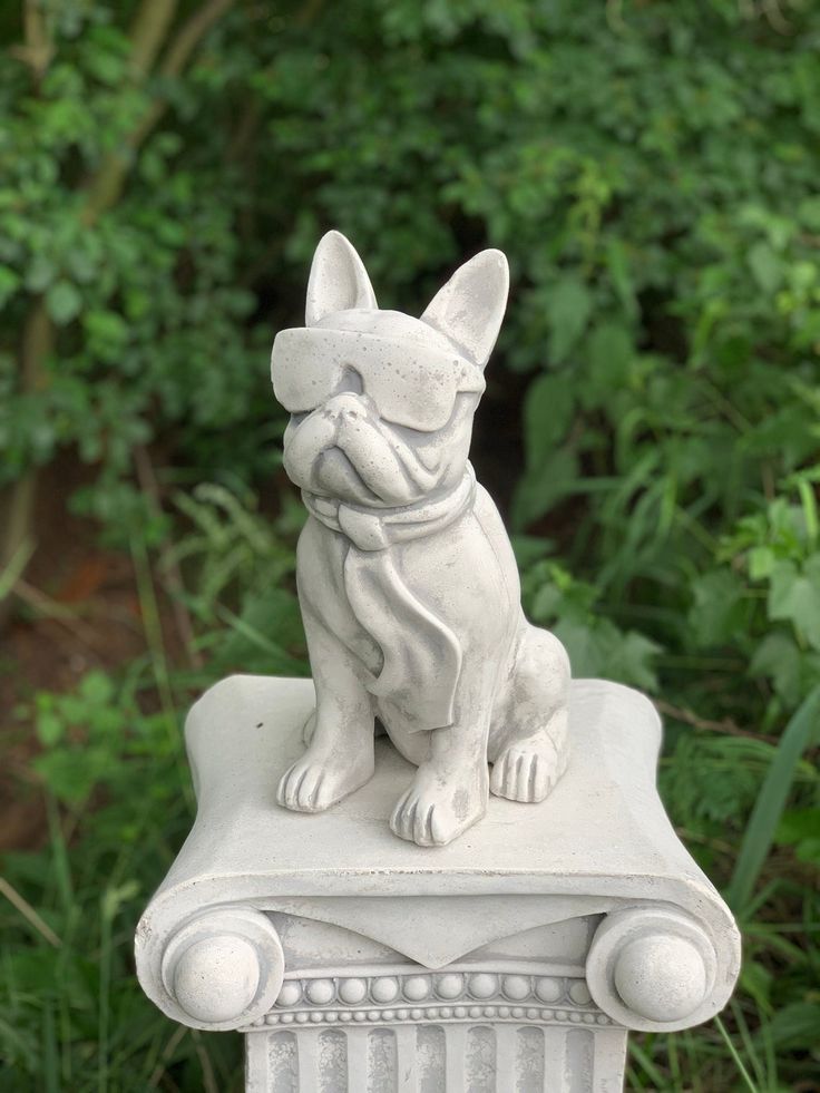 a statue of a dog sitting on top of a white column in front of some bushes