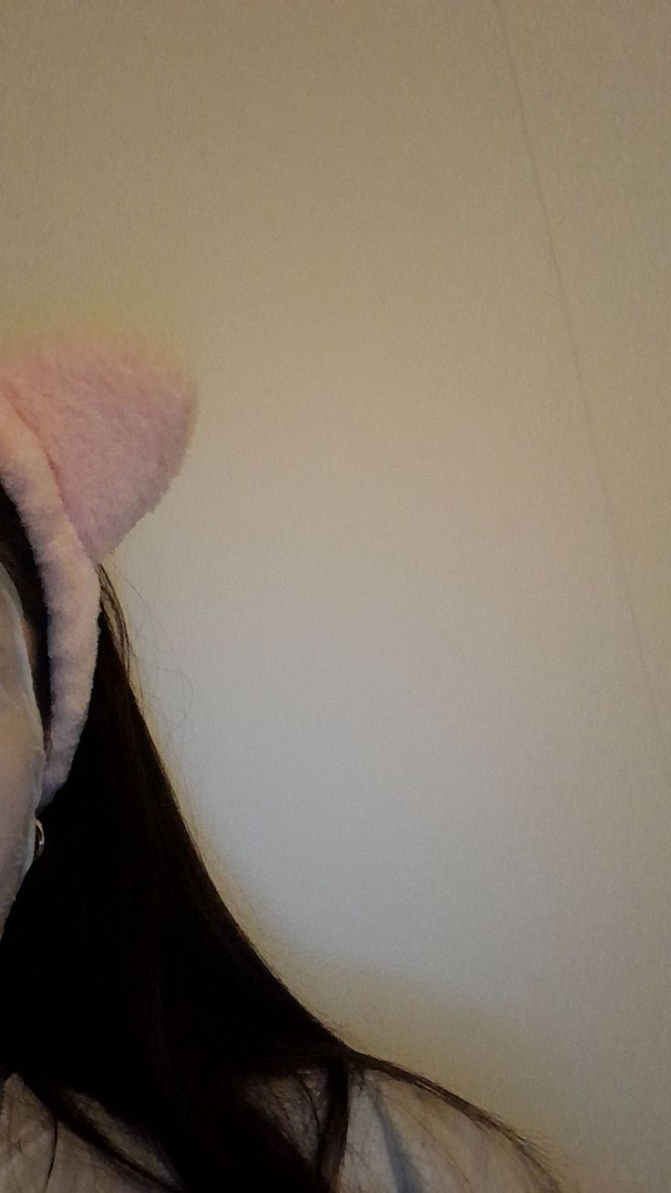 a woman with long hair wearing a pink cat ear muffs on top of her head