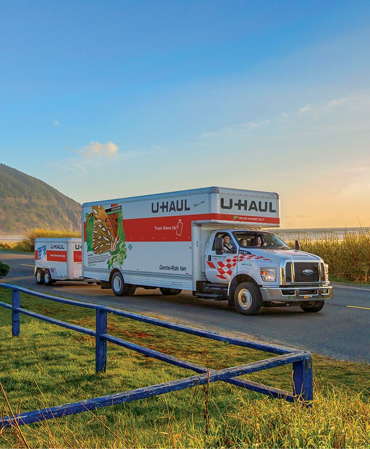 a delivery truck driving down the road near a fence and grassy area with mountains in the background