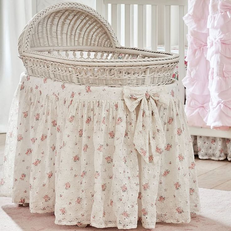 a white crib with pink ruffles and flowers on the bedding is shown