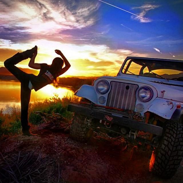 a woman doing yoga in front of an old jeep with the sun setting behind her