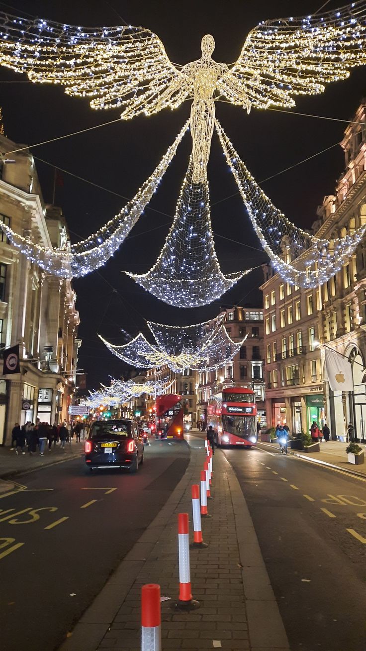 an angel statue is lit up in the middle of a city street at christmas time