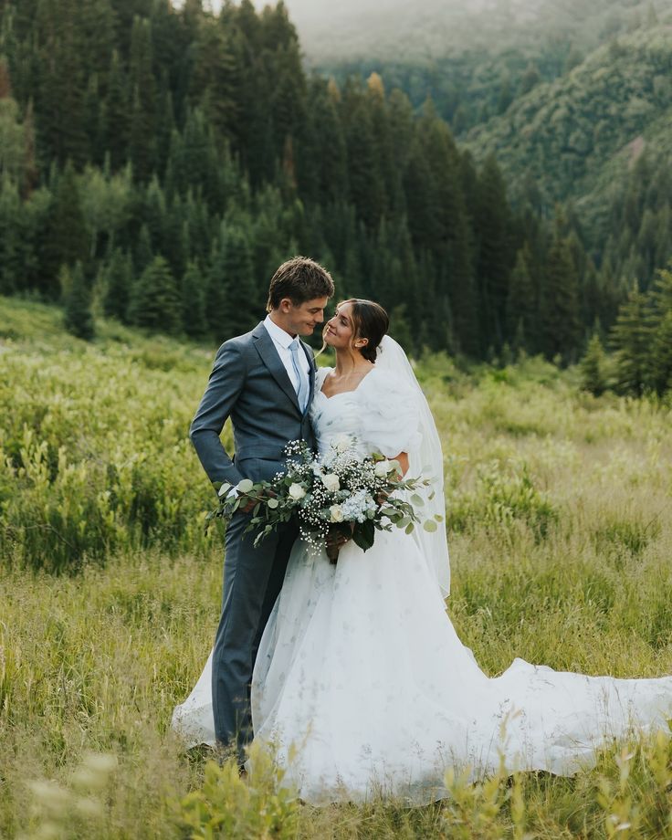 a bride and groom are standing in the grass with mountains in the backgroud