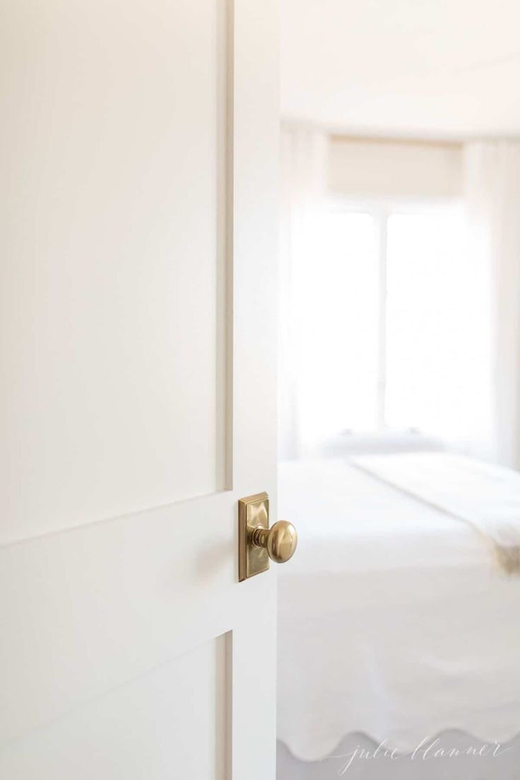 an open door leading to a bed in a room with white walls and carpeting