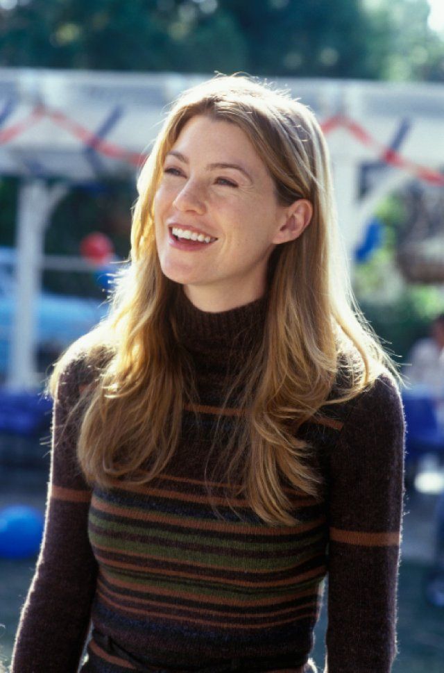 a woman with long blonde hair smiling and wearing a striped turtle neck sweater in front of a building