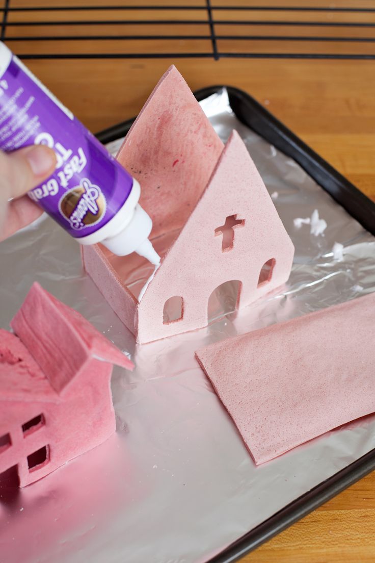 someone is decorating a house with pink icing and glue on a tray next to it