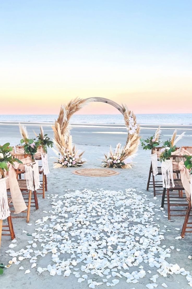 an outdoor ceremony set up on the beach with white petals and greenery in front of it