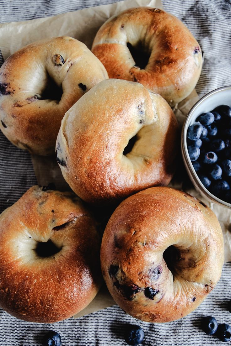 bagels and blueberries are on a cloth next to a small bowl of fruit