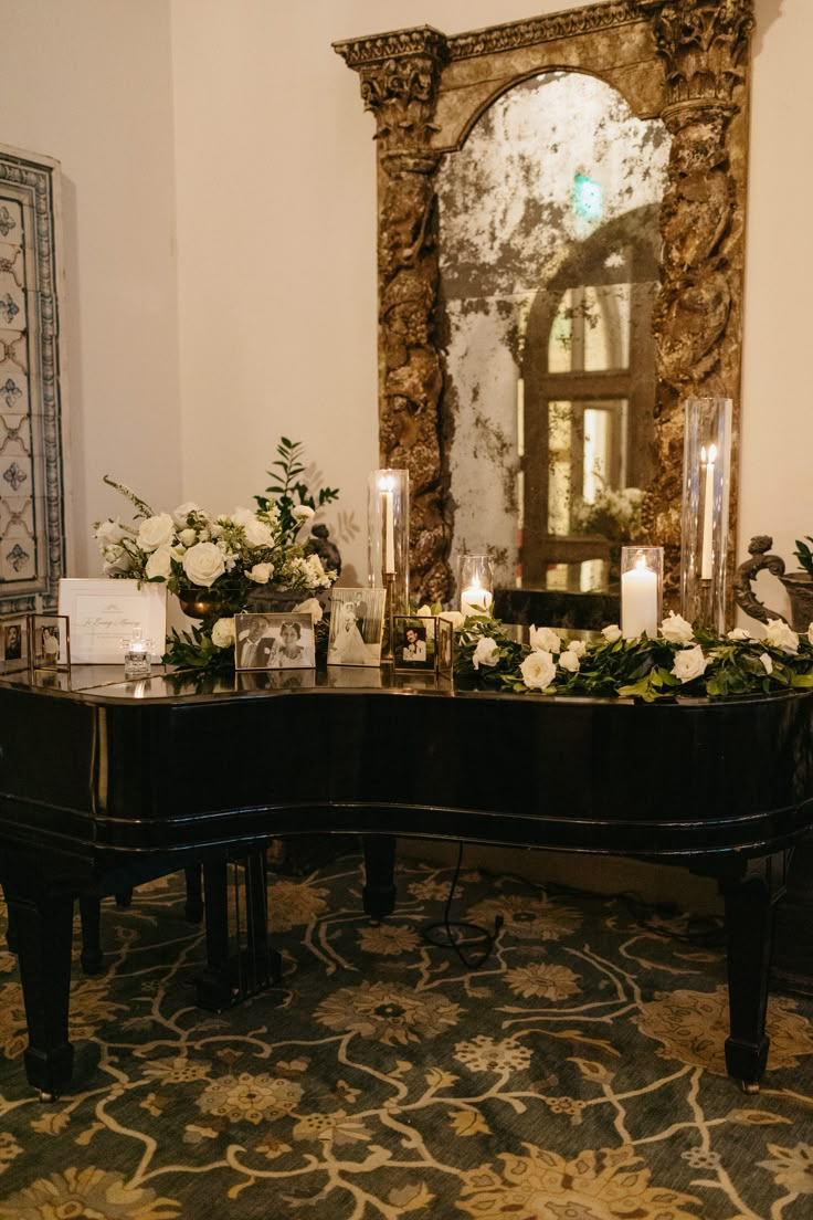 a grand piano with flowers and candles on it in front of a mirror, decorated with greenery