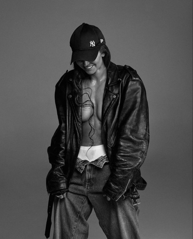 a shirtless man in black leather jacket and hat posing for a photo with his hands on his hips