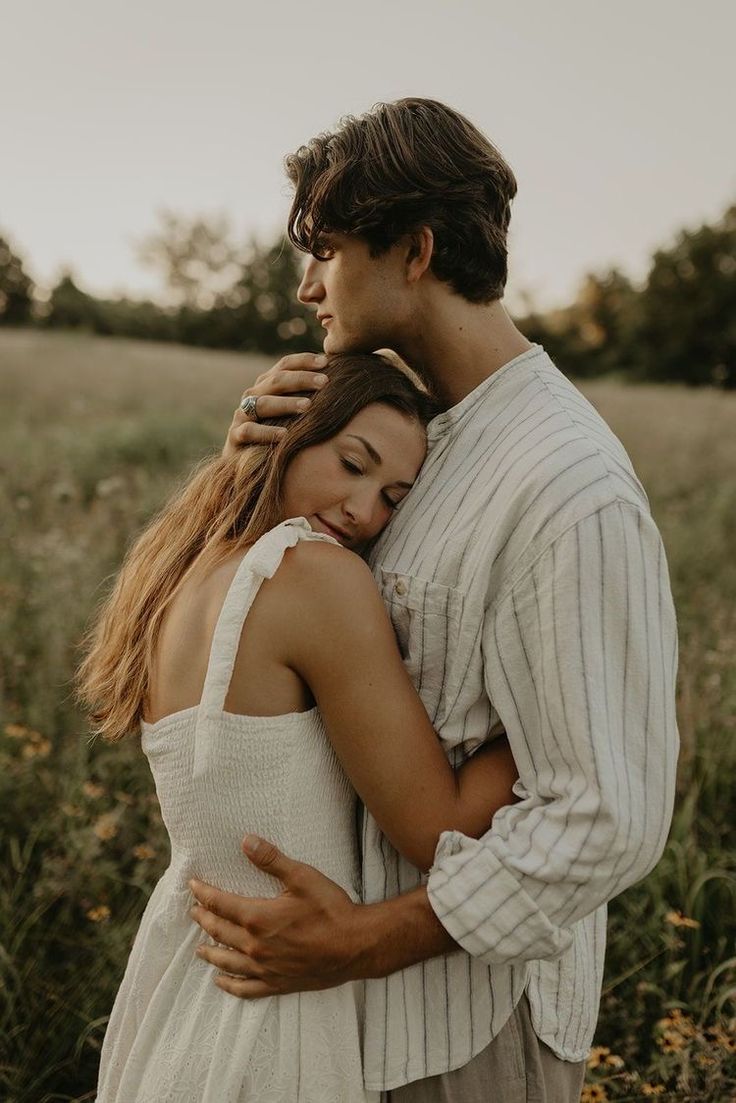 a man and woman embracing each other in the middle of a field with tall grass