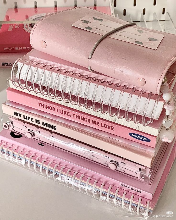 a stack of pink notebooks sitting on top of a white table next to a pile of books