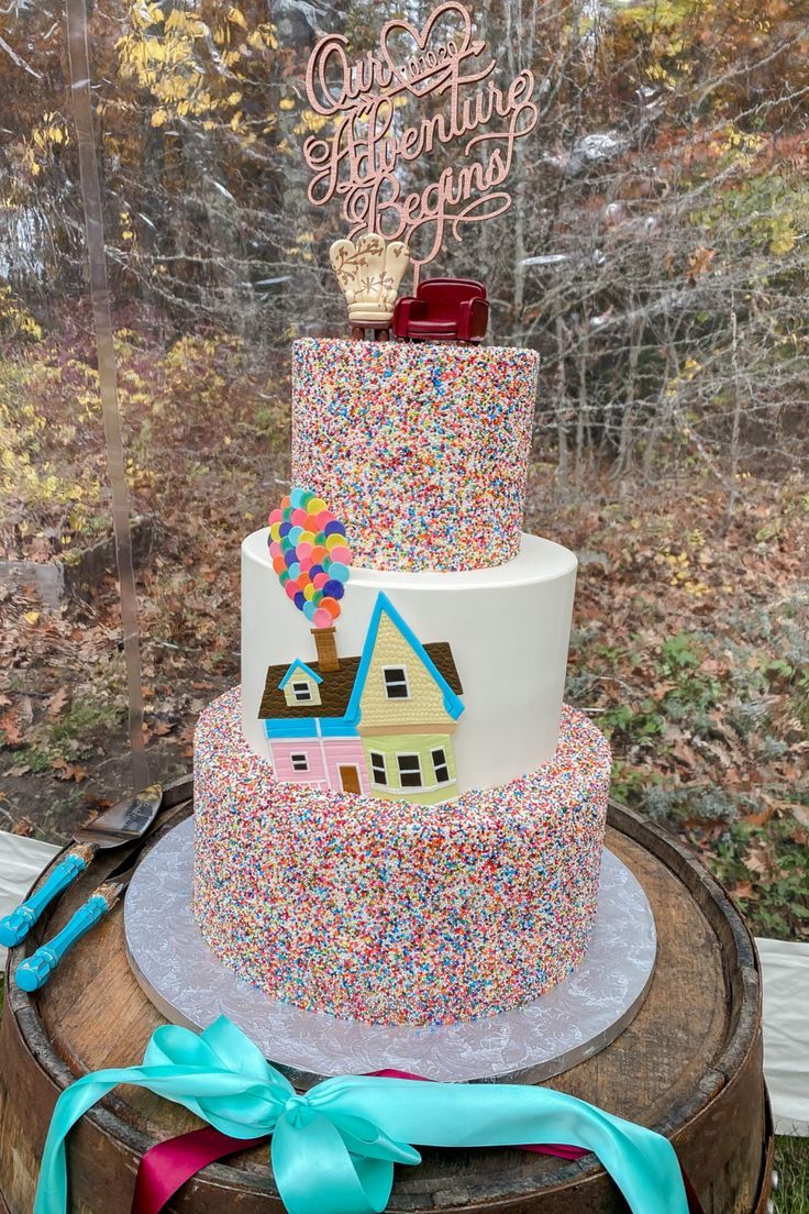 a three tiered cake with colorful sprinkles and a house on top