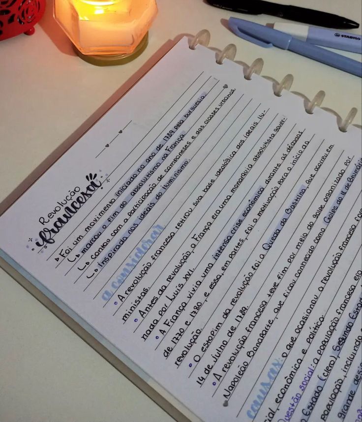 a notepad sitting on top of a table next to a candle and some pens