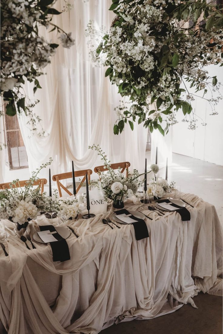 the table is set up with white flowers and black ribbon sashes on it, along with candles