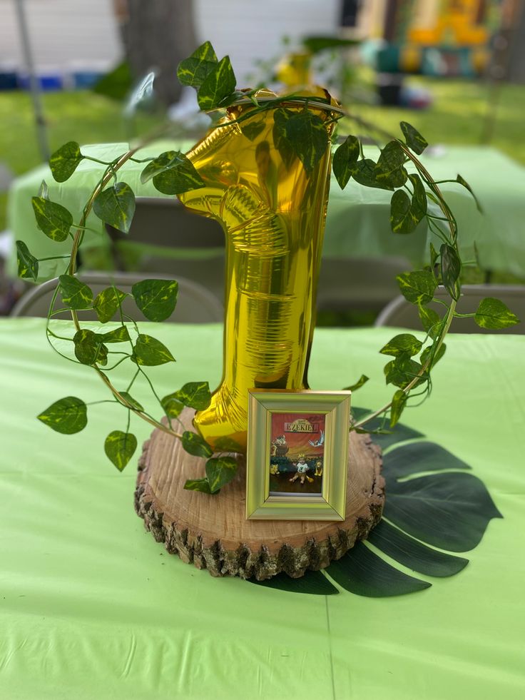 a yellow vase sitting on top of a wooden stump next to a framed photo and green leaves