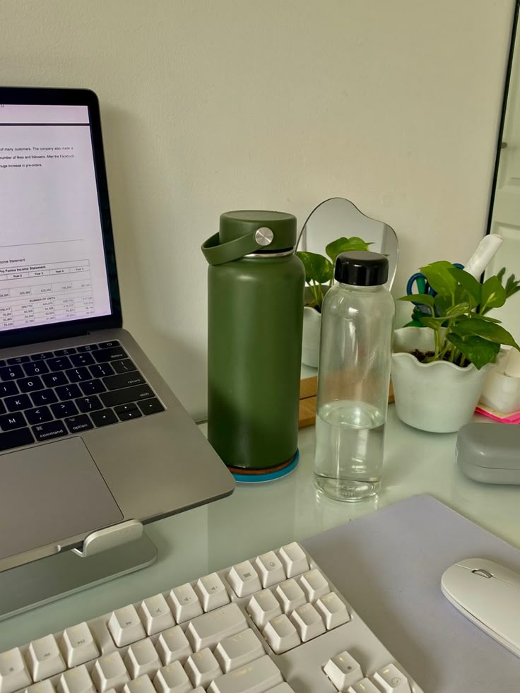 a laptop computer sitting on top of a desk next to a keyboard and cup filled with water