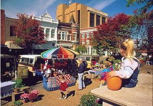 people are shopping at an outdoor market in front of some tall buildings and colorful trees