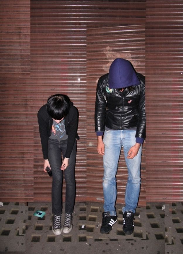 two people standing next to each other in front of a wall with closed shutters